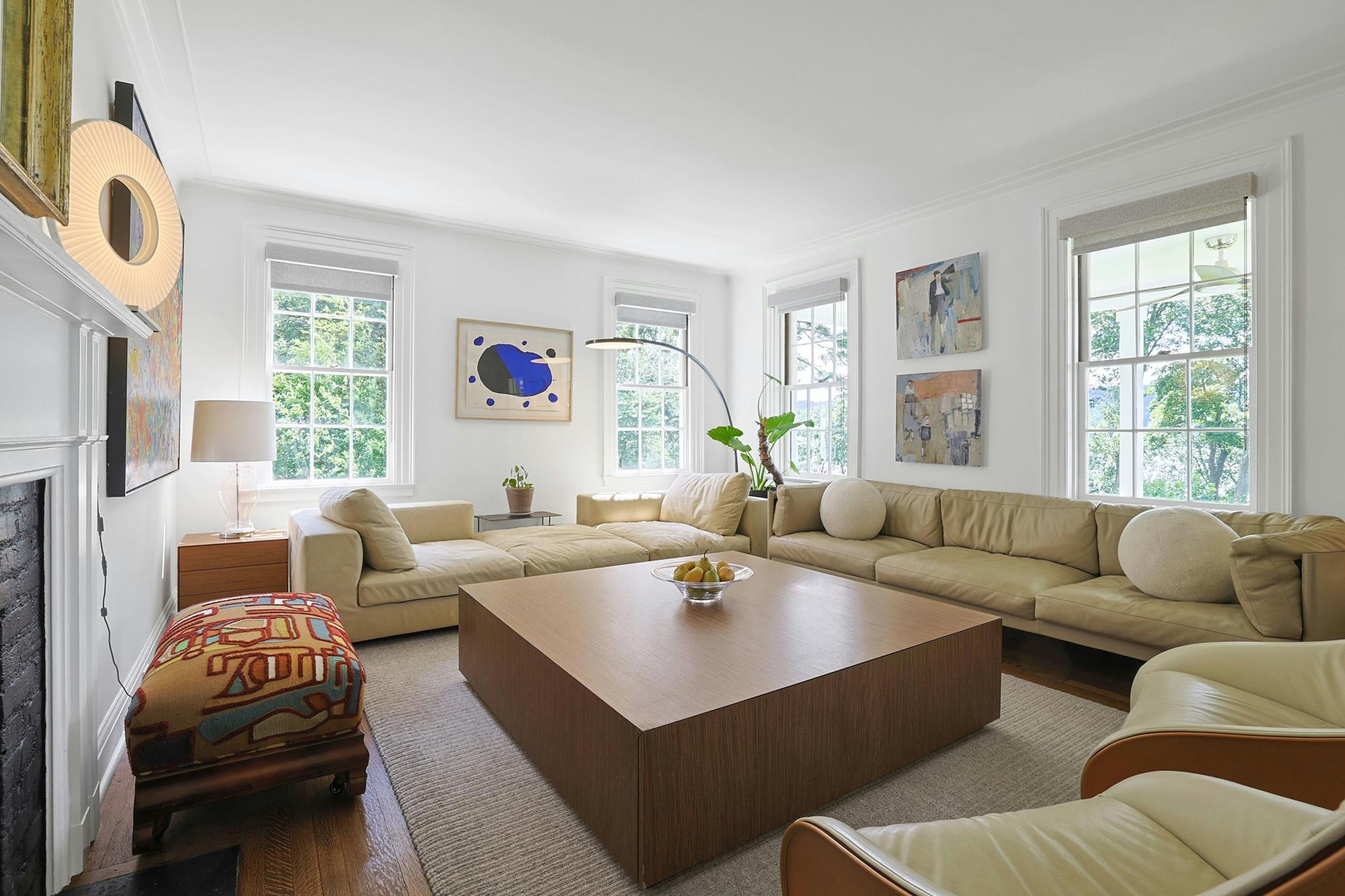 Living room with a low-profile leather sectional, modern art, and four windows onto the trees.