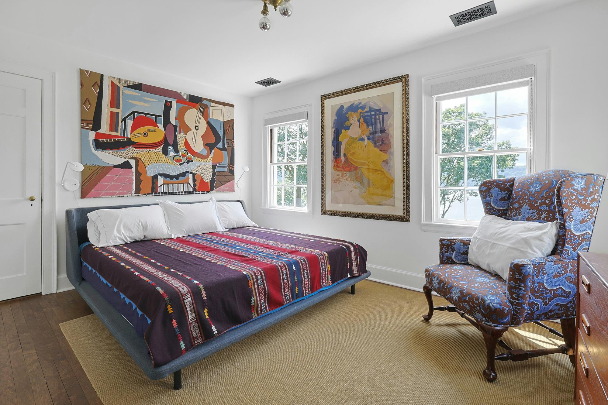 A serene bedroom with Marimekko poppy bedding, an antique armoire, and an abstract painting.
