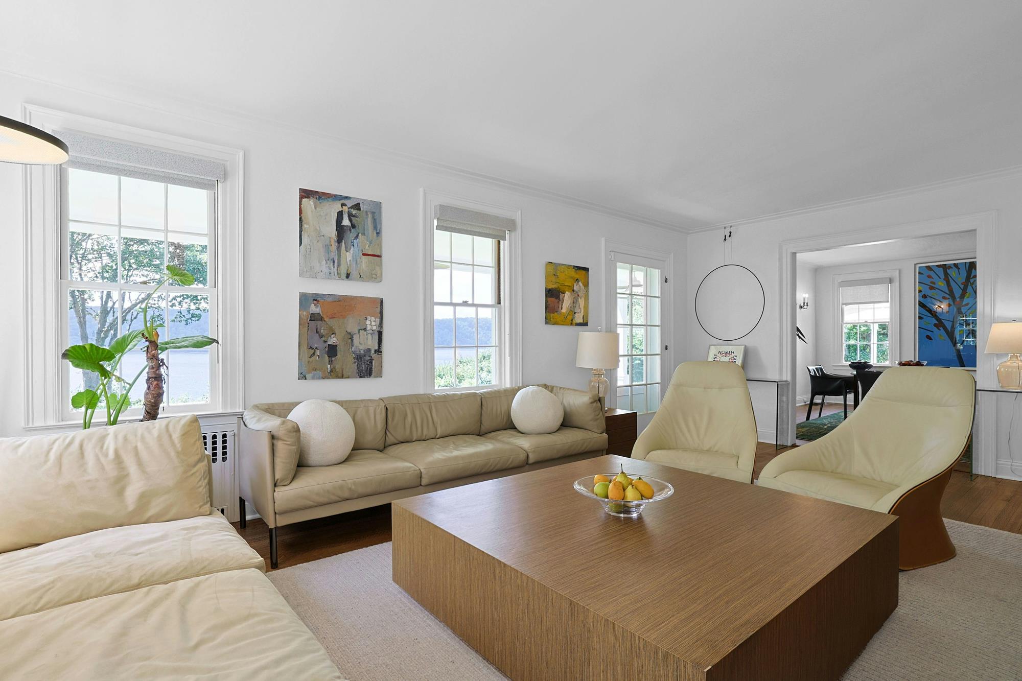 Long living room with tan leather sofas, oak coffee table, and river-side windows opening onto the dining room.